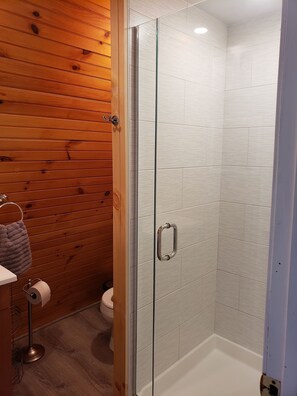 Un baño con paneles de madera, cabina de ducha de vidrio, inodoro y perchero para toallas.
