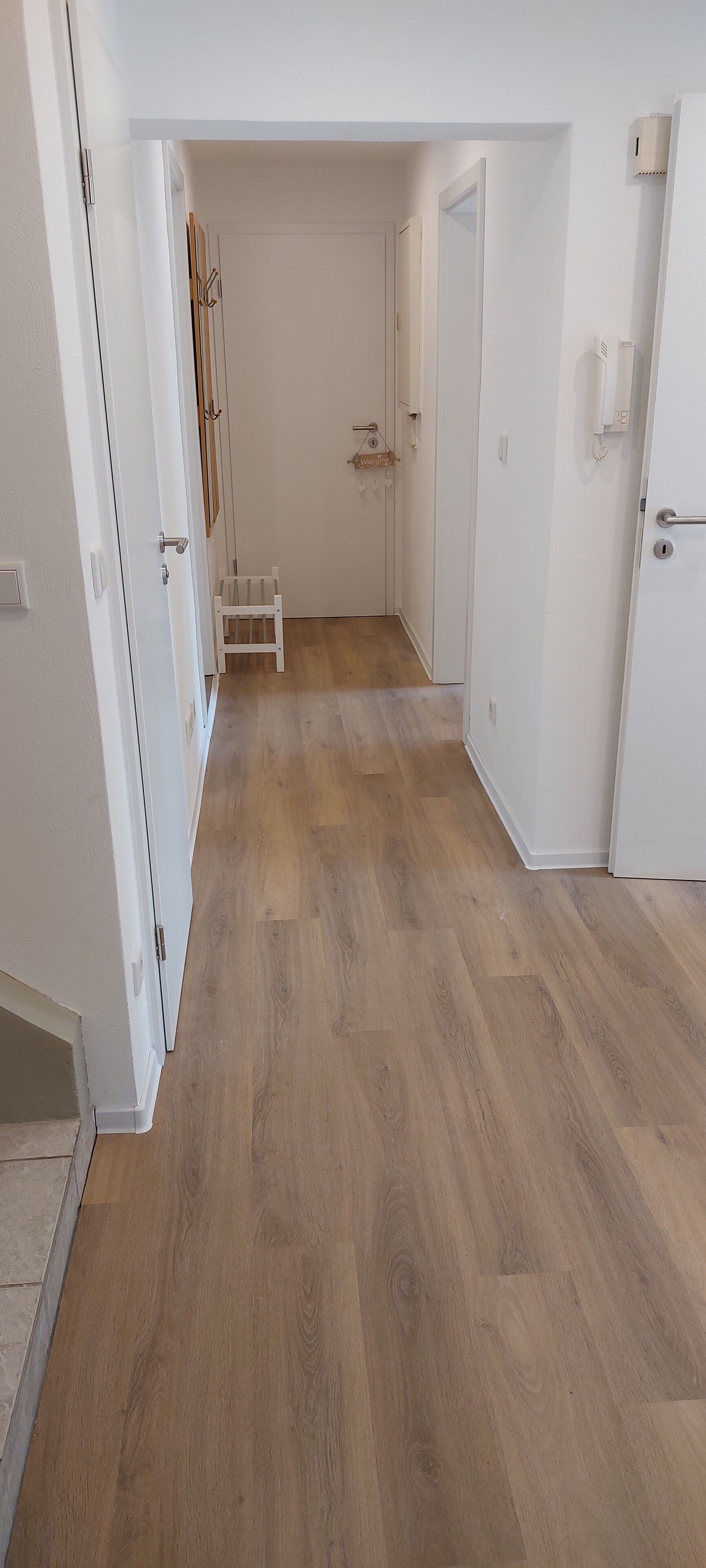 Un couloir avec un plancher en bois, des portes blanches et une petite chaise blanche.