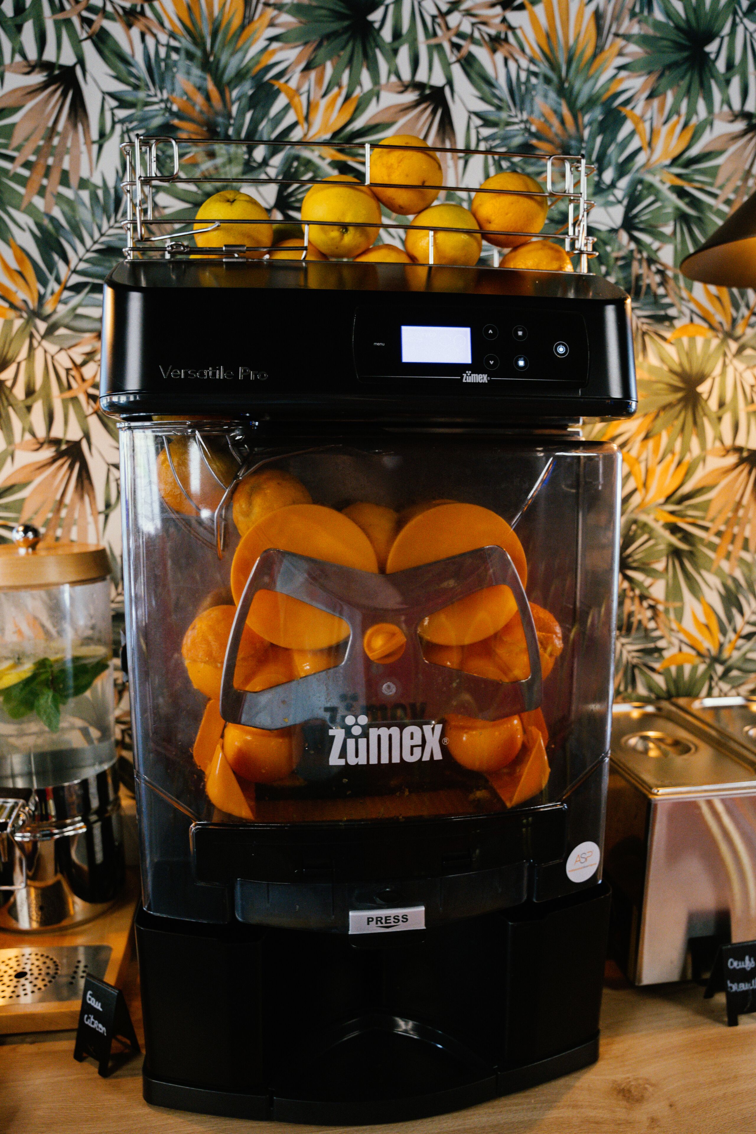 A black juicer with a transparent container filled with sliced oranges.