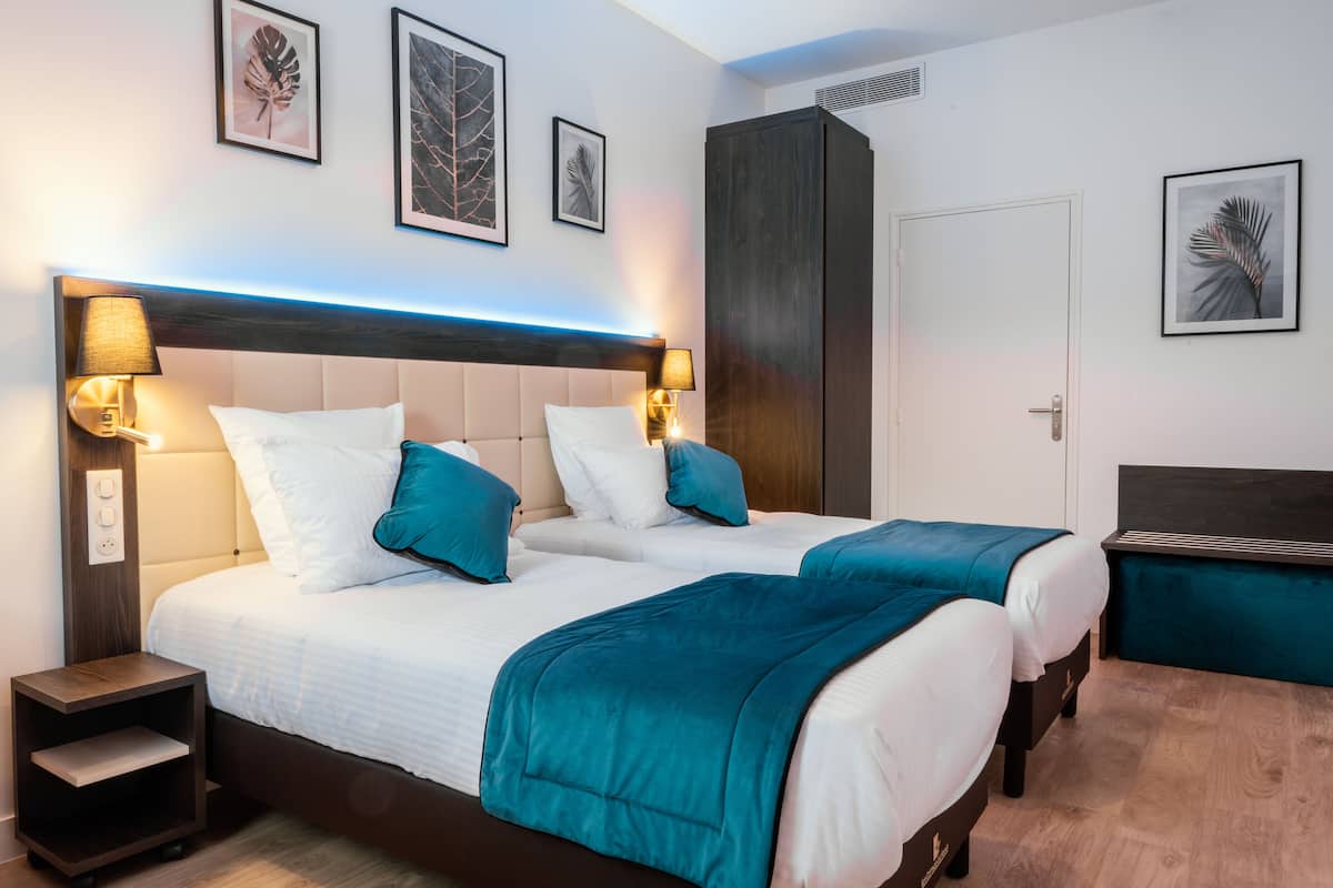 A double bed with teal bedding, two bedside lamps, and a nightstand.
