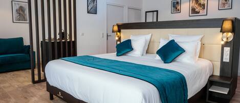 A modern hotel room with a large bed, teal bedding, a dark headboard, and wall-mounted lamps.