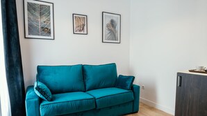 A teal sofa in a room with a wooden floor, a dark cabinet, and three framed leaf artworks on the wall.