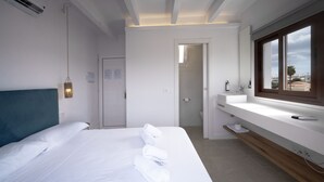 A modern hotel room with a bed, a bathroom with a sink and mirror, and a view of the outside. - Hostal Castell de Lô (Alayor)