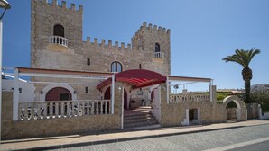 A historic stone building with a red awning, a balcony, and a palm tree nearby. - Hostal Castell de Lô (Alayor)