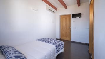 Un dormitorio con una cama, una puerta de madera y un televisor en la pared.