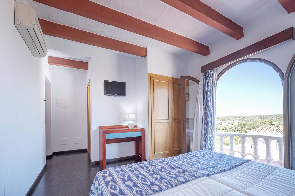 A bedroom with a bed, a desk, a TV, and a balcony with a view.