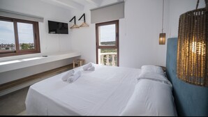 A hotel room with a large bed, a TV mounted on the wall, and a balcony with a view of the city. - Hostal Castell de Lô (Alayor)