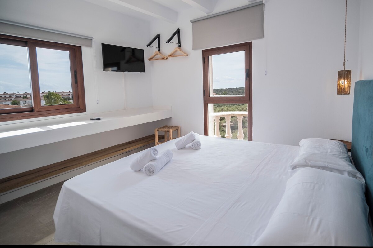 A hotel room with a large bed, a TV mounted on the wall, and a balcony with a view of the city.