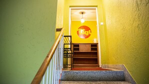 A staircase with a handrail leading to a room with a yellow wall and a circular logo. - Tiglkåk - Hostel (Rauma)
