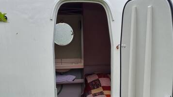 A van with an open door revealing a small sleeping area with a red mat, a quilt, and a round mirror on the wall.