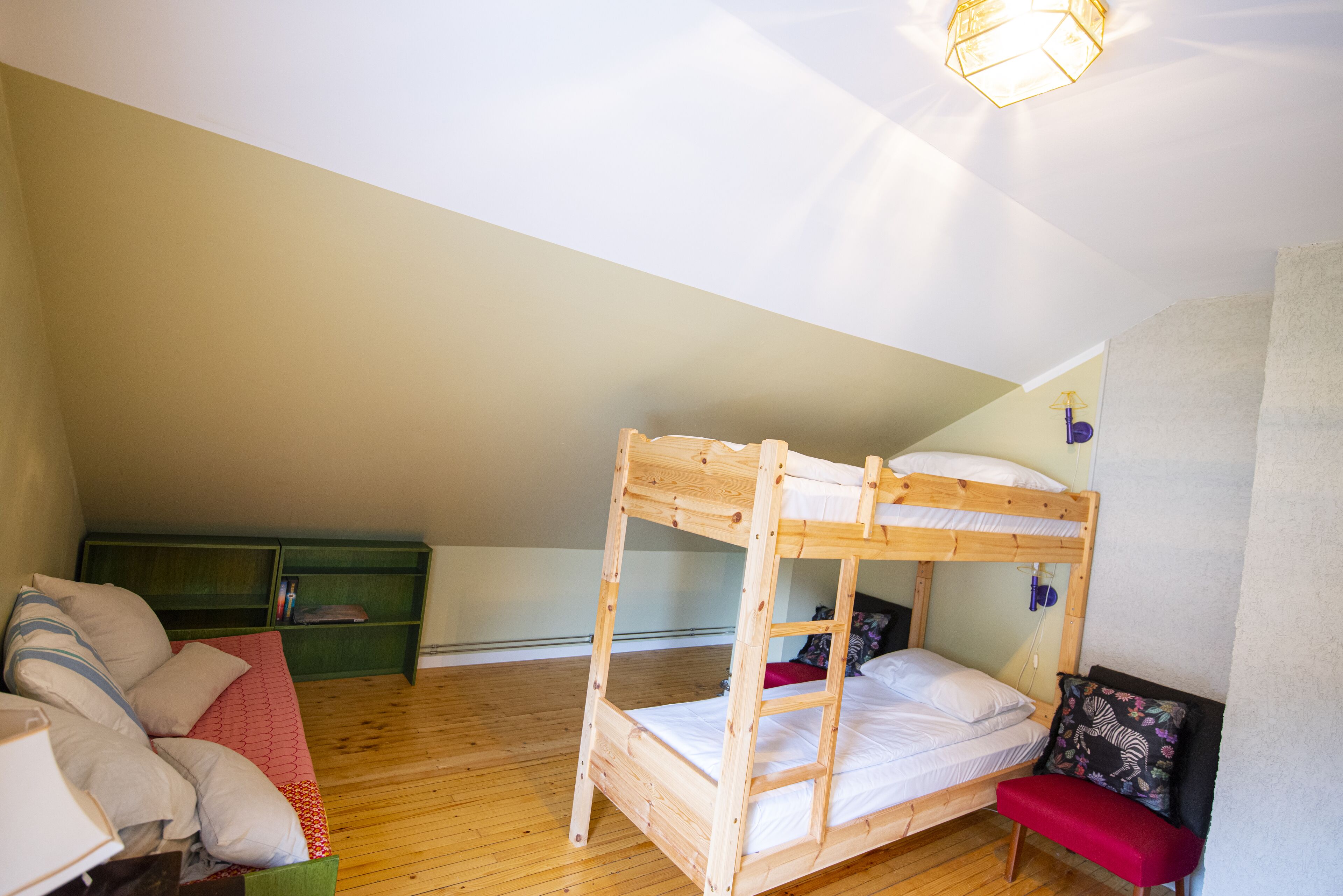 A bunk bed with a ladder, a green sofa, and a red bench in a room with wooden flooring and a sloped ceiling.