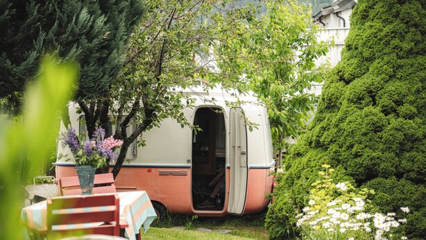 A vintage camper parked in a lush garden with a table and chairs nearby. - Tiglkåk - Hostel (Rauma)