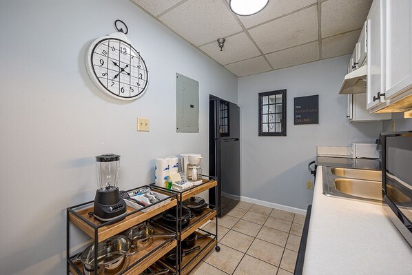 A kitchen with a clock, a refrigerator, a sink, and a wooden rack with kitchenware.