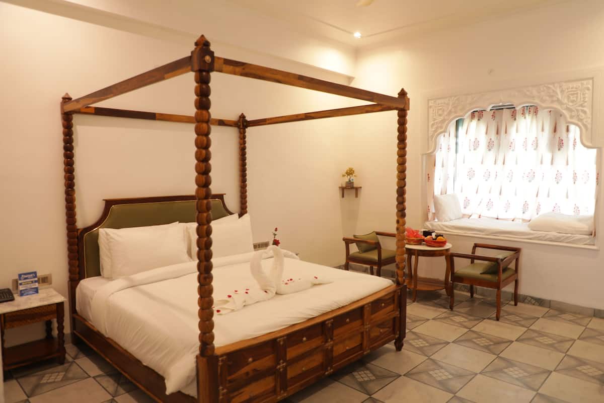 A four-poster bed with a wooden frame, a bedside table, a chair, and a window with patterned curtains.