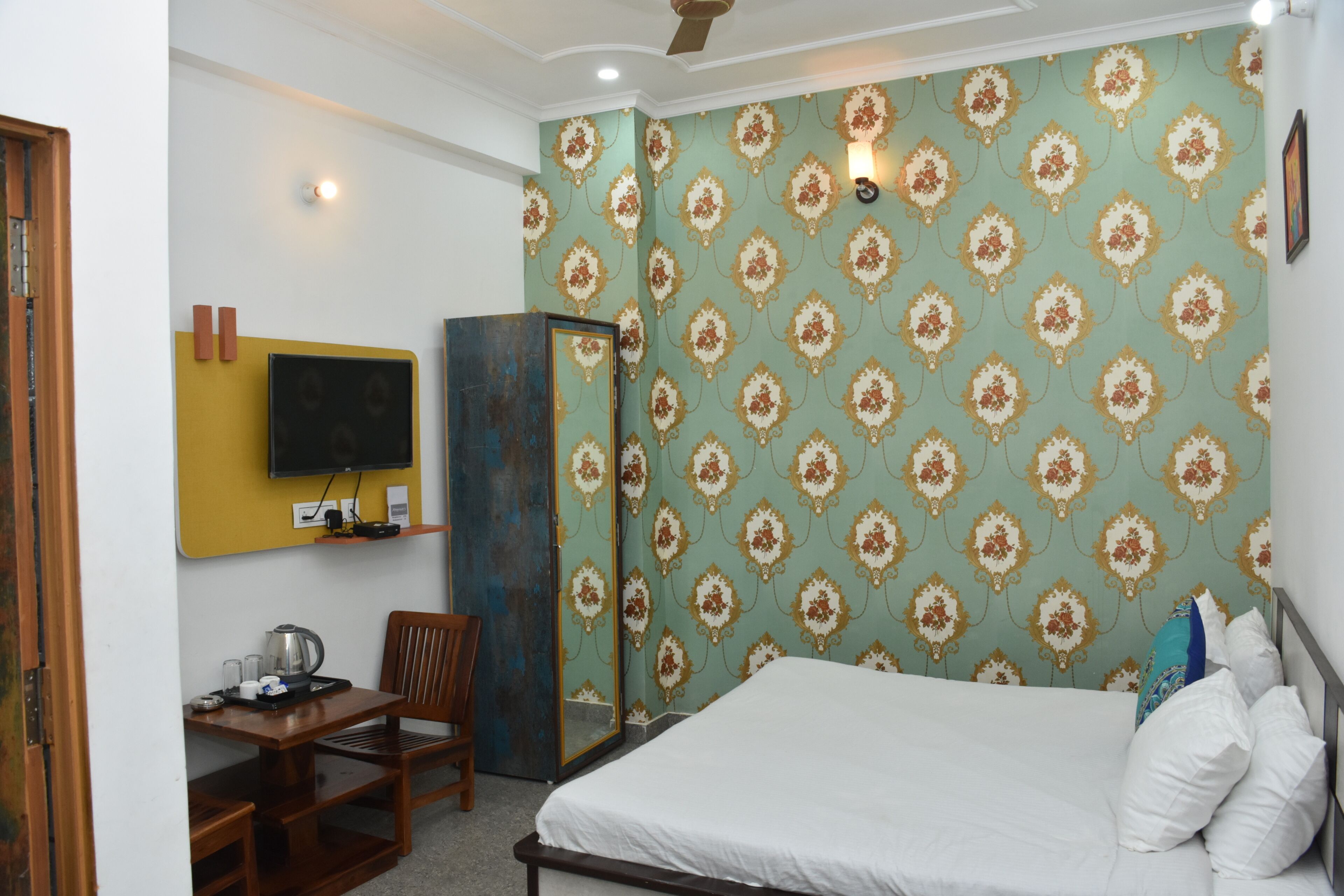 A hotel room with a bed, a desk with a chair, a television, and a wardrobe.