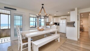 Een moderne keuken met witte kasten, een eettafel met banken en uitzicht op de oceaan door grote ramen.