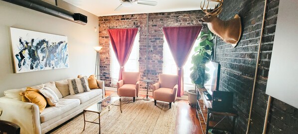 Un salon avec un canapé blanc, deux fauteuils, une table basse, une cheminée et une tête de cerf accrochée au mur.