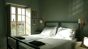 Uma cama bem arrumada com lençóis brancos, uma cabeceira de madeira e uma janela com persianas.