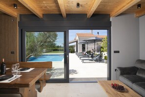 Ein modernes Interieur mit einem Holzespeisetisch, gedeckt für zwei Personen, einer Couch und Blick auf einen Außenpool und eine Lounge-Bereich.