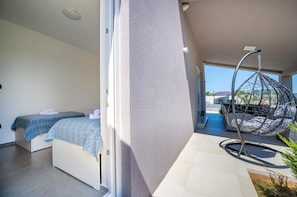 A modern bedroom with two beds, a hanging chair, and a view of the outside.