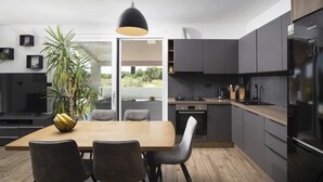 A modern kitchen with dark cabinets, a wooden dining table, and a large window offering a view of greenery. - Holiday house Ana (Fažana)