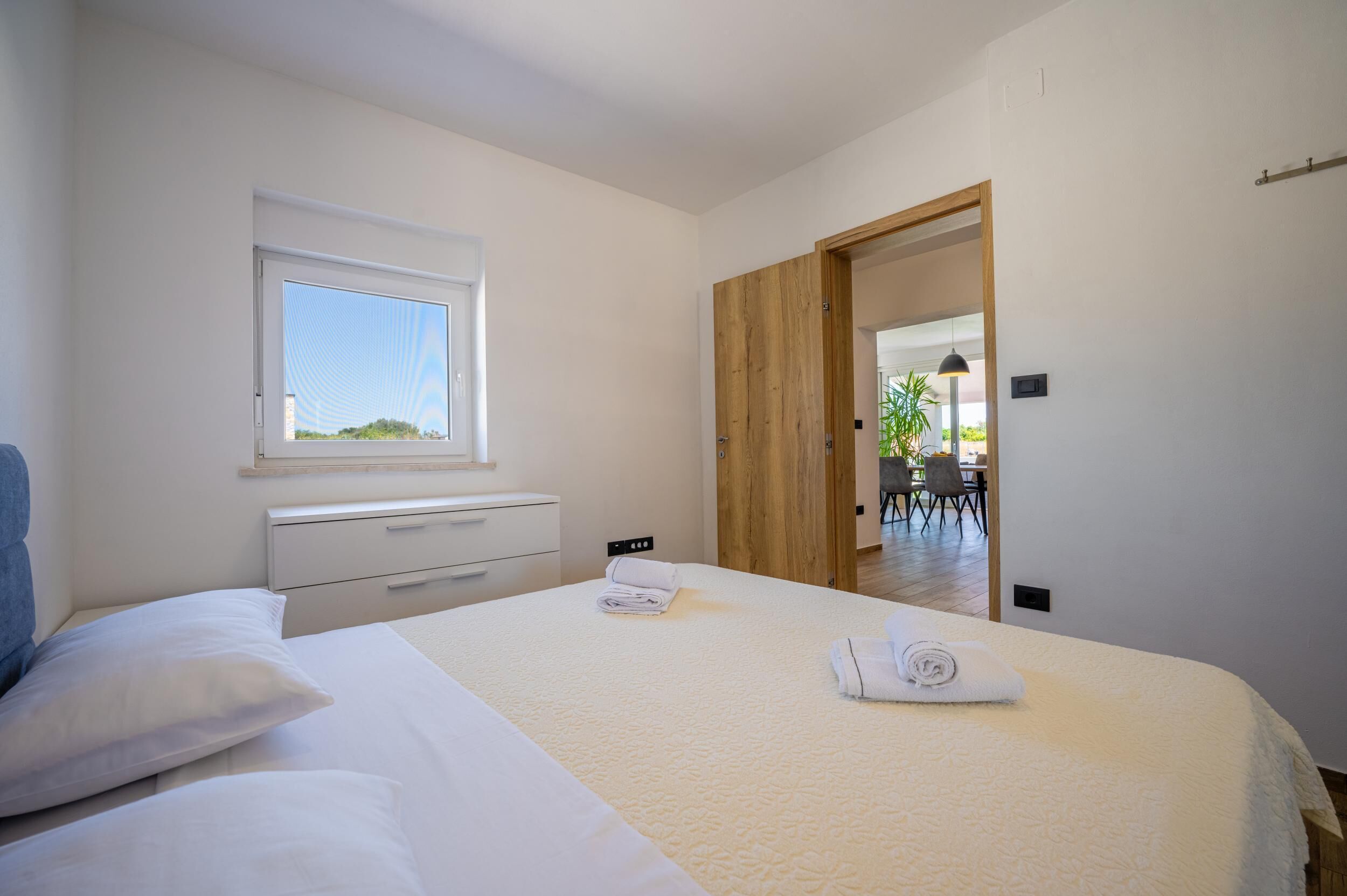Une chambre avec un lit bien fait, une fenêtre, une porte en bois et une vue sur un coin repas.