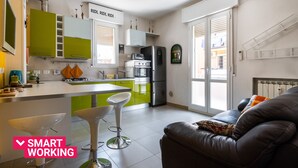 Une cuisine moderne avec des meubles de couleur verte, un réfrigérateur et un coin repas comprenant une table blanche et deux tabourets de bar.