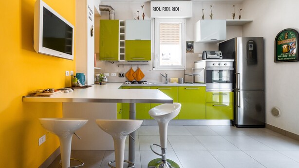 Une cuisine moderne avec un mur d’accent jaune, des armoires vertes, un réfrigérateur en acier inoxydable et un four encastré.