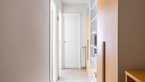 Un couloir avec une porte blanche au fond, une bibliothèque et une petite étagère en bois.