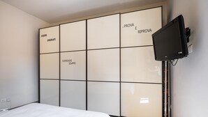 Une chambre à coucher avec un lit, un téléviseur fixé au mur et une armoire dont les portes sont ornées d’inscriptions en italien.