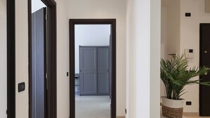 Un couloir avec une porte donnant sur une pièce, une plante en pot posée sur une petite table et un thermostat fixé au mur.