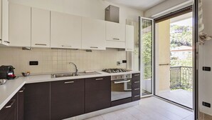 Une cuisine moderne avec des meubles de couleur sombre, un plan de travail blanc, une cuisinière à gaz et une grande fenêtre.