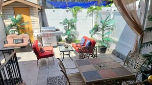 Un patio al aire libre con una mesa de comedor, dos sofás rojos y una parrilla.