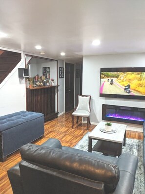 Ett vardagsrum med en tv, en blå soffa, en lädersoffa, en vit stol och ett litet bord med en växt.