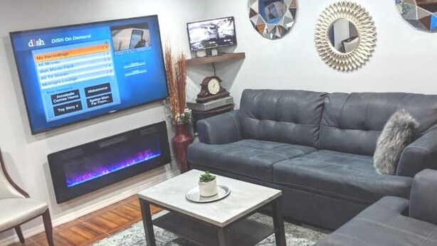 Una sala de estar moderna con un sofá gris, una mesa de centro, un televisor de pantalla plana, espejos decorativos y una chimenea.