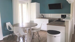 Une cuisine moderne avec des meubles blancs, une table à manger entourée de chaises blanches et un petit îlot central doté d’une poubelle.