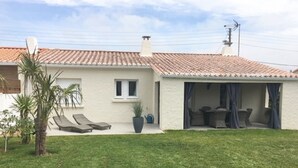 Une maison de plain-pied avec un toit en tuiles, un petit patio avec une table et des chaises, et une pelouse.