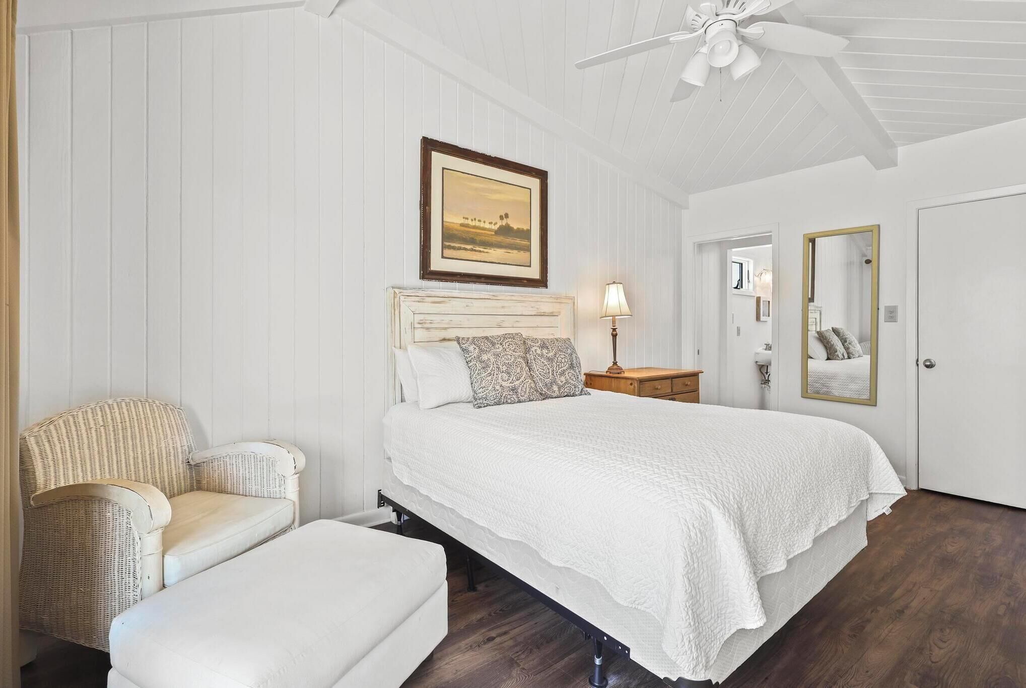 Ein Schlafzimmer mit Bett, Stuhl, Nachttisch, Lampe und Spiegel.