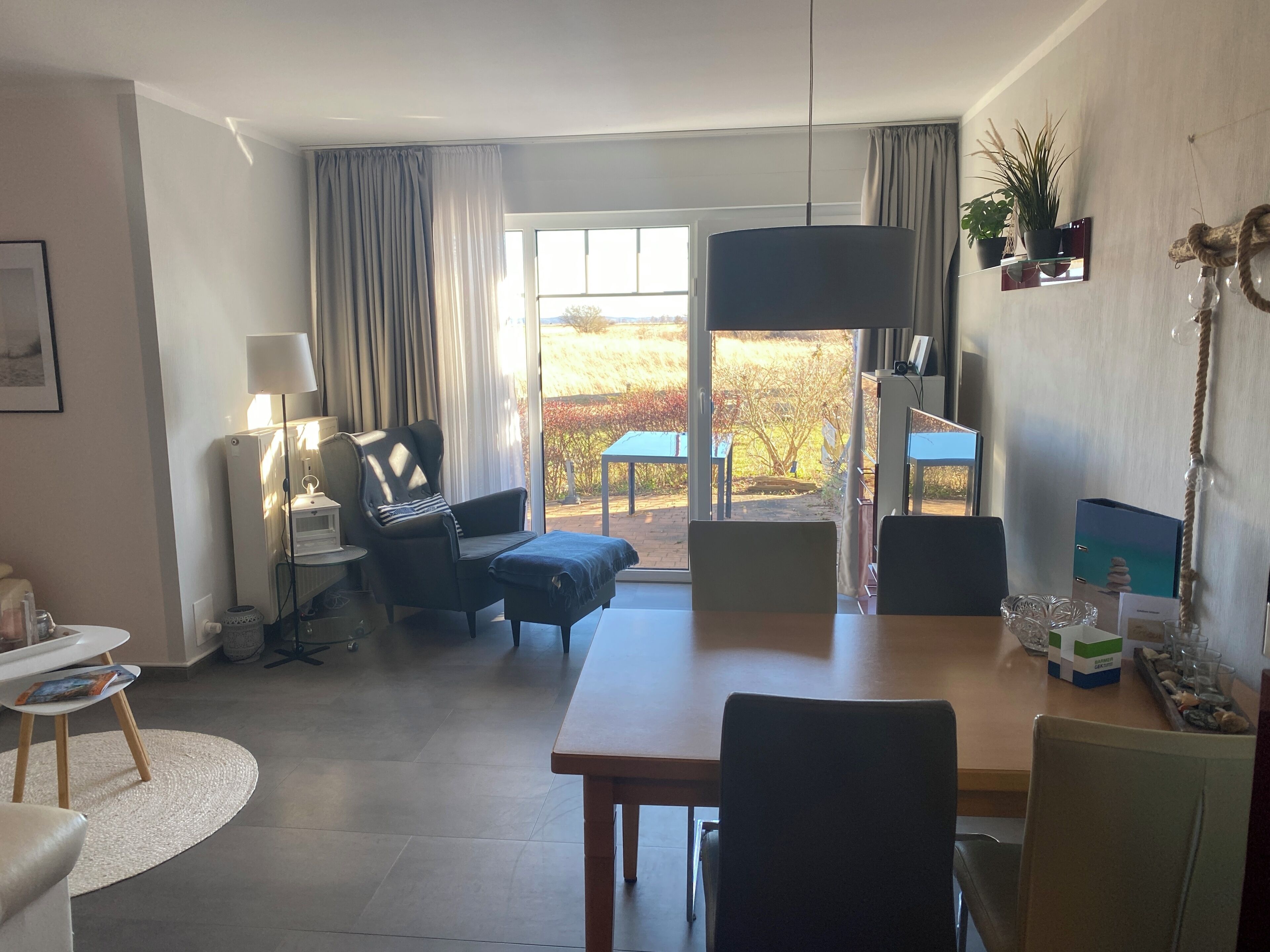 Ein modernes Wohnzimmer mit Essbereich, einem großen Fenster mit Vorhängen, einer Couch, einer Lampe und einer Zimmerpflanze.
