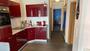 A modern kitchen with red cabinets, a stainless steel oven, and a countertop with various appliances and utensils.