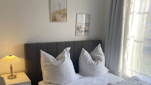 A neatly made bed with white bedding, a bedside lamp, a nightstand with a lamp, and two framed pictures on the wall.