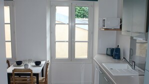 A kitchen with wooden floors, white cabinets, a sink, and a window. - Charming apartment ideally located (Bayeux)