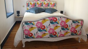 A bed with a floral headboard, two pillows, and a bedside table with a lamp. - Charming apartment ideally located (Bayeux)