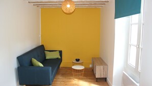 A room with a blue sofa, a small round table, and a wooden cabinet. - Charming apartment ideally located (Bayeux)