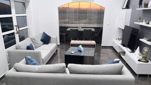 A modern living room with a sofa, coffee table, and a view of the sunset over the water.