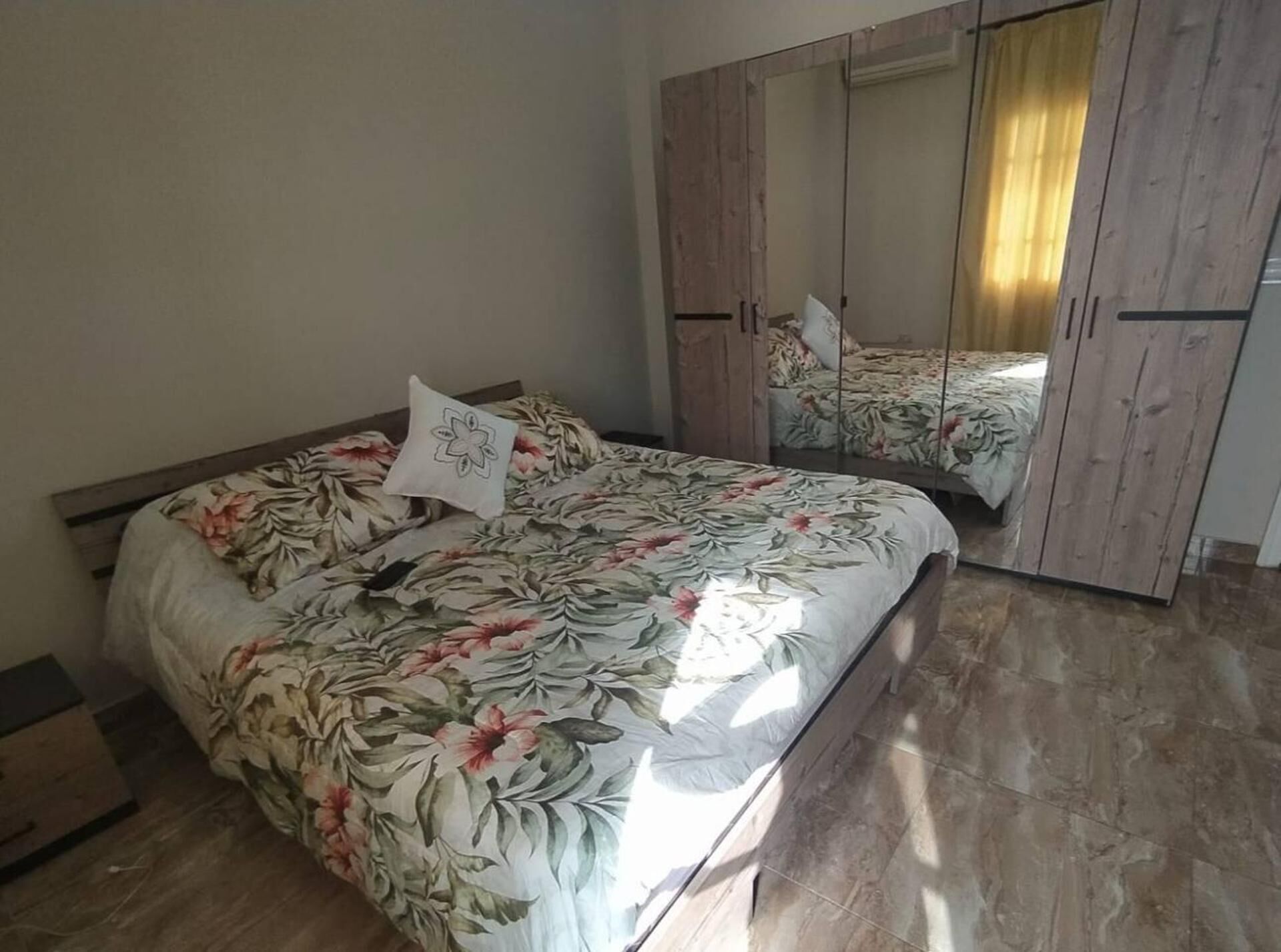 Un dormitorio con cama, ropa de cama floral, un armario y un espejo.