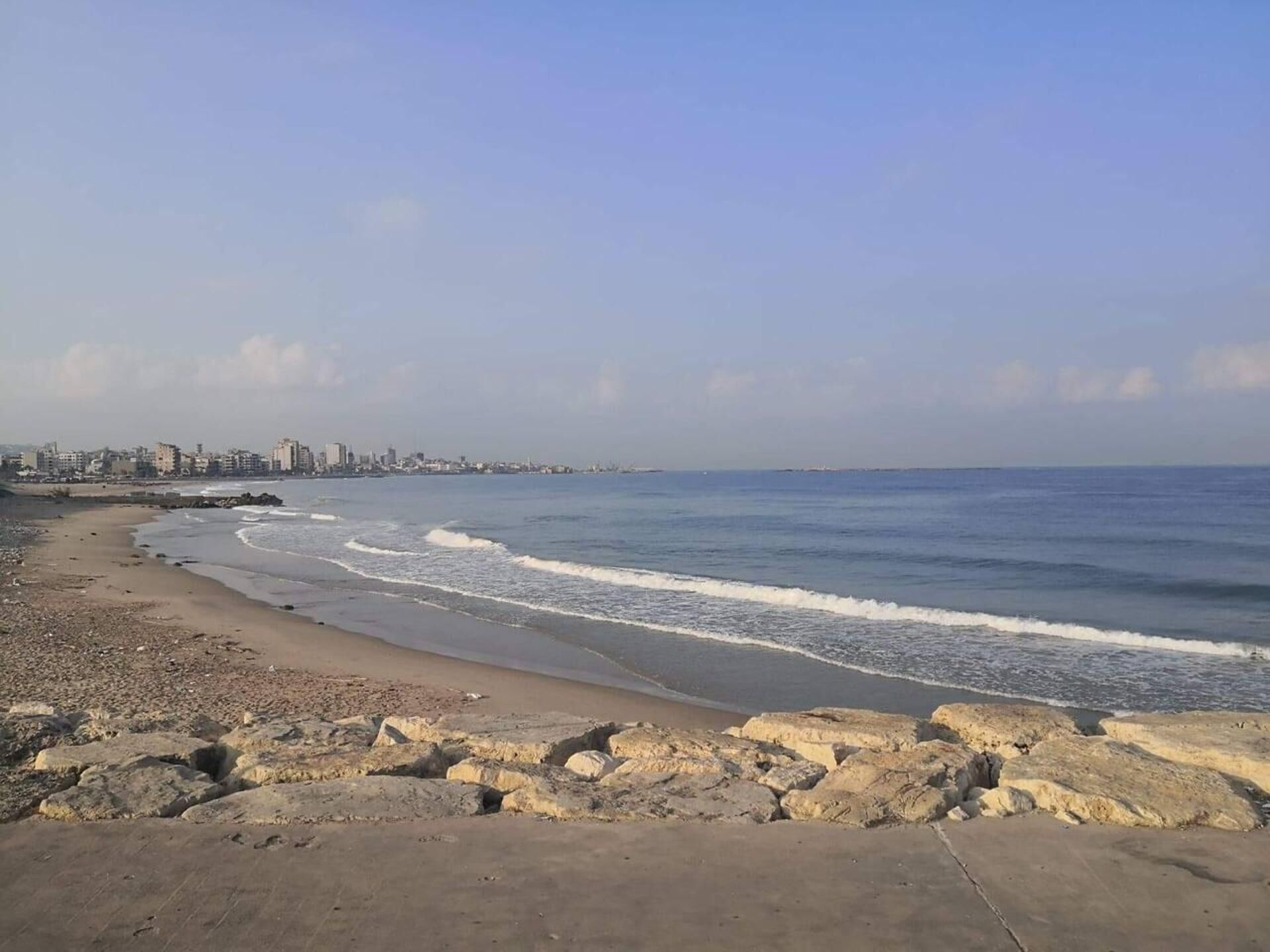 Ein Strand mit felsigem Ufer und einer Stadtlandschaft im Hintergrund.