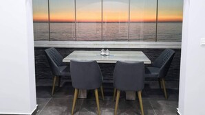 A dining area with a table and two chairs, a view of the sea at sunset, and a tiled floor.