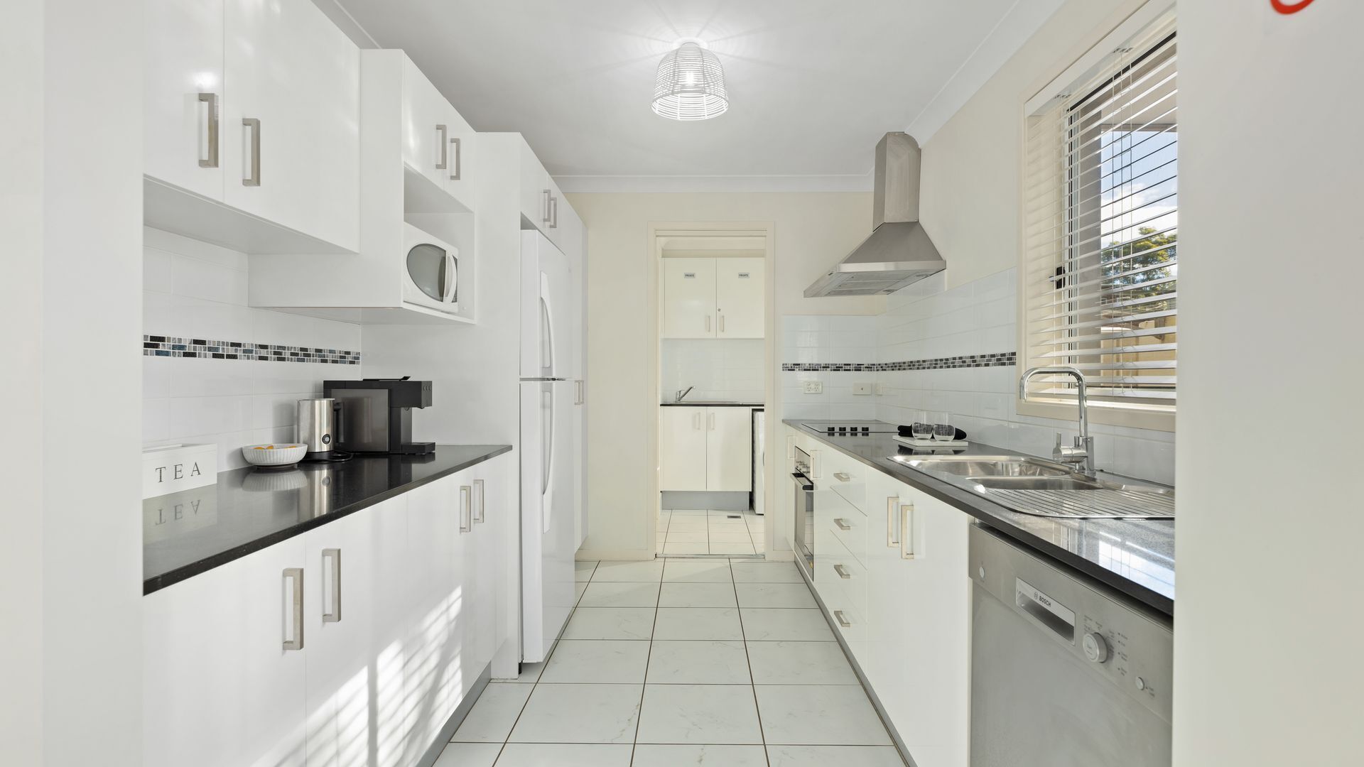 A modern kitchen with white cabinetry, a black countertop, and a stainless steel sink.