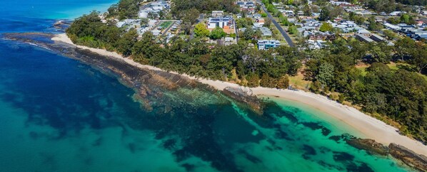 An aerial view of Jervis Bay with a coastal area, clear blue waters, and a residential zone with houses and greenery.